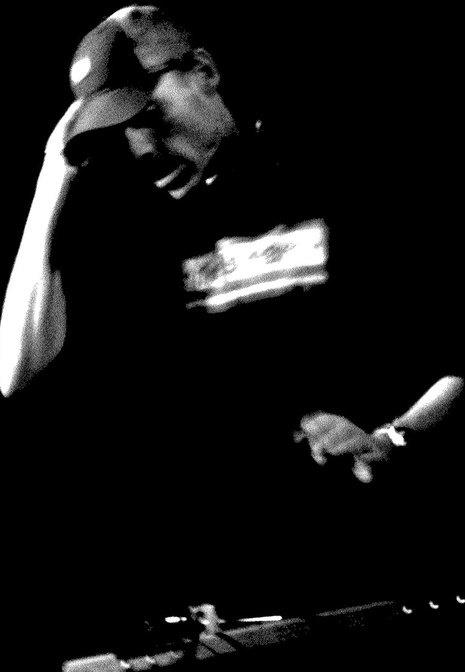 High-contrast black and white portrait of DJ Natural Nate® with hand on headphones under stage light